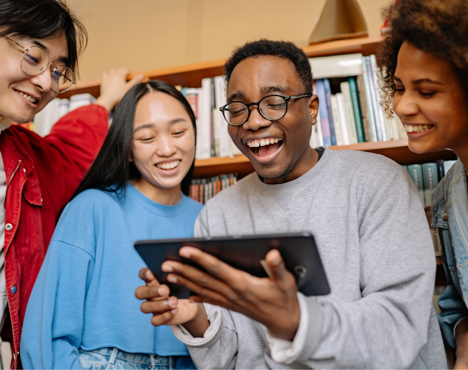 Four students laughing together while looking at a tablet in a library
