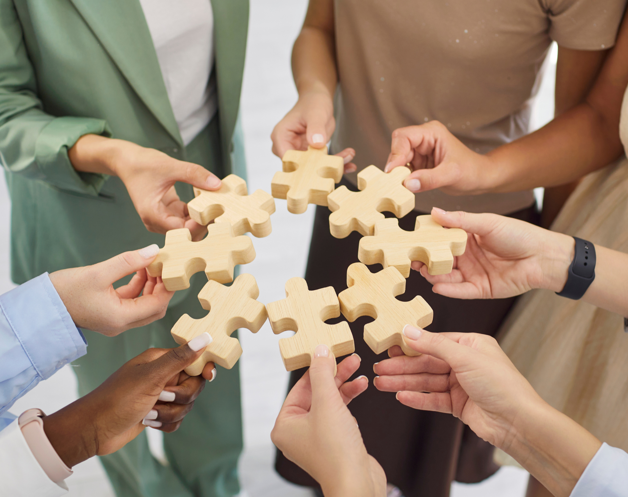 Diverse group of hands joining wooden puzzle pieces together, symbolizing sharers coming together